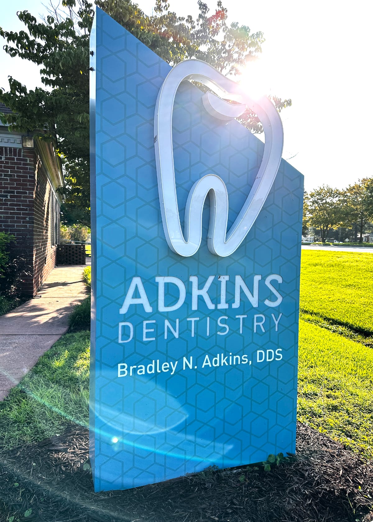 Adkins Dentistry sculpted blue monument sign with halo-lit tooth logo, sun behind
