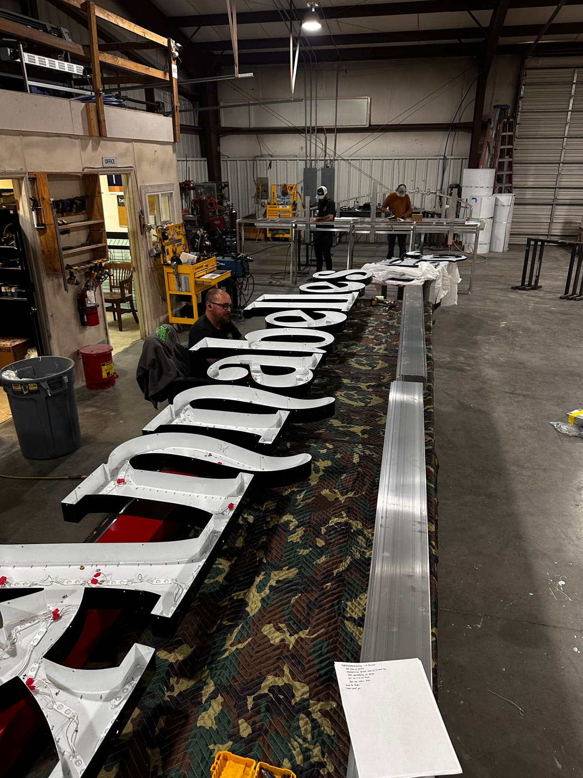 Giant script channel letters for Annabelle’s laid out on the fabrication floor with crew at work