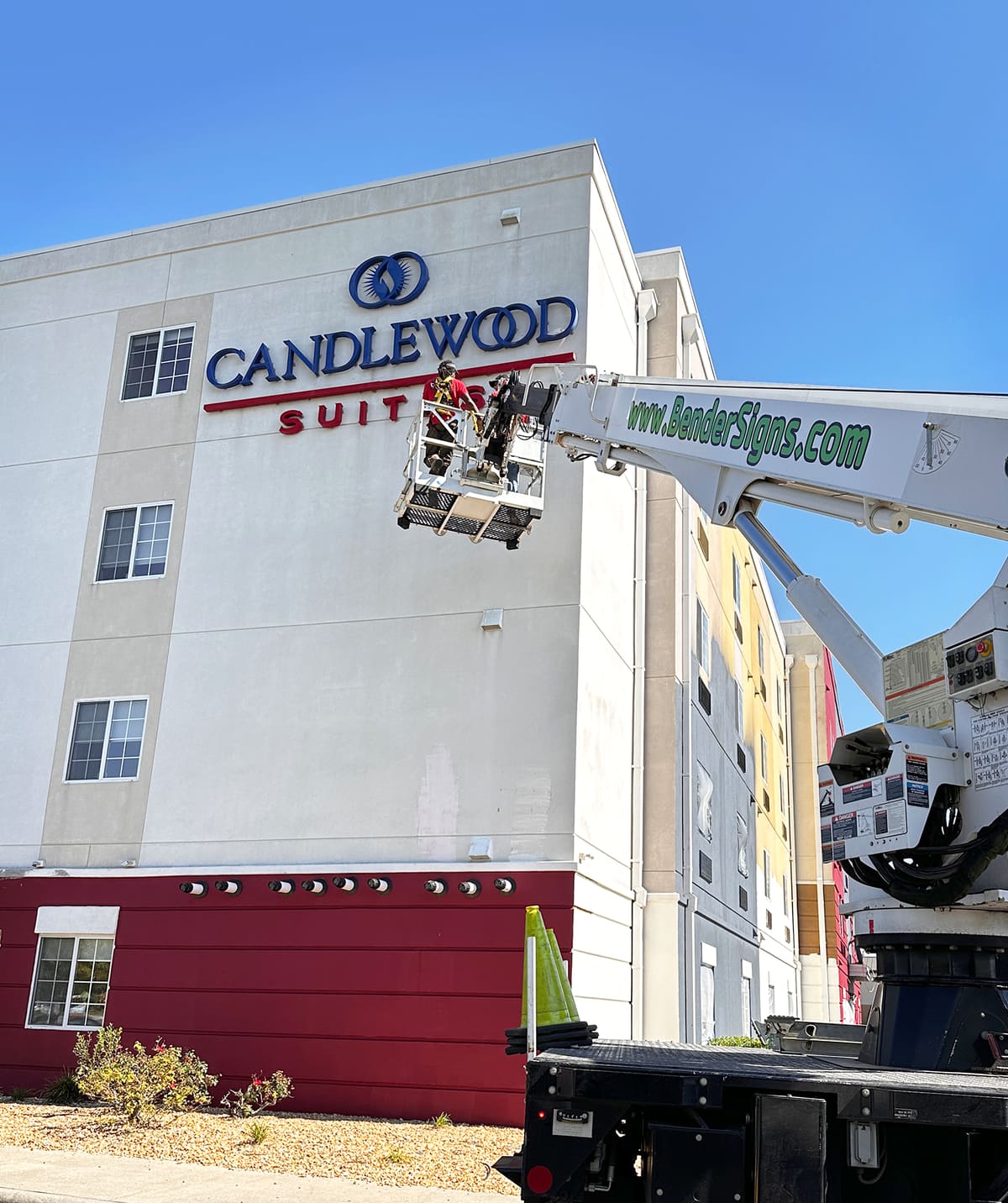 Installer in a bucket lift mounting Candlewood Suites letters with the Bender crane arm across the sky
