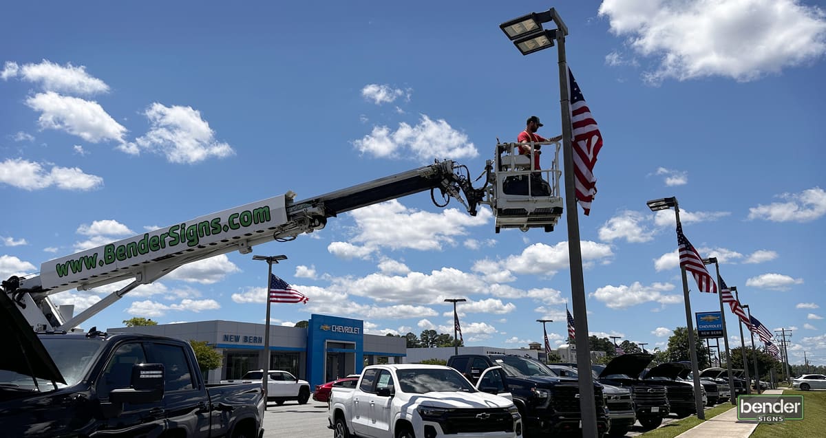 Bucket-truck worker mounting American flags on light poles at a Chevrolet dealership