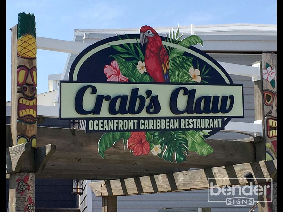 Crab’s Claw Oceanfront Caribbean Restaurant carved-look oval sign with parrot artwork