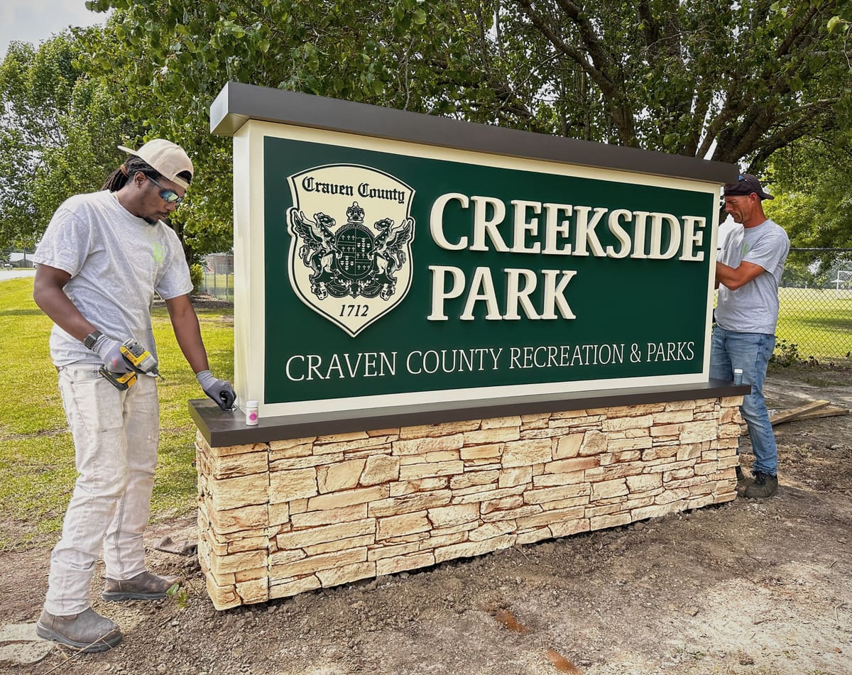 Two Bender Signs crew members finishing the Creekside Park stone-base monument sign for Craven County