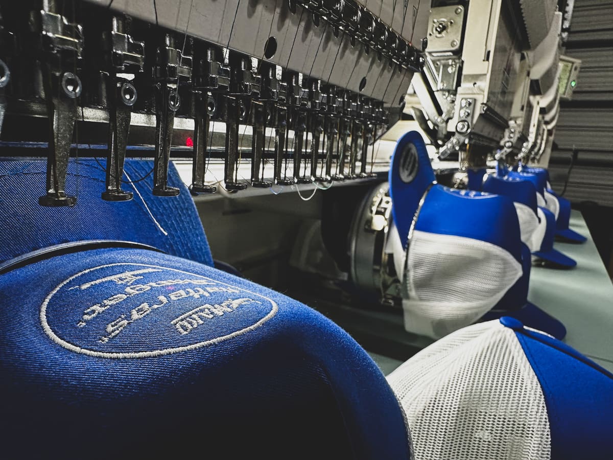 Embroidery machine stitching blue trucker caps at Bender Apparel