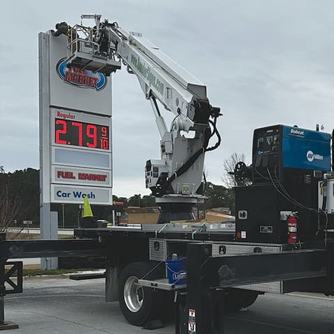 Bender crane truck servicing a fuel station price sign with LED digits