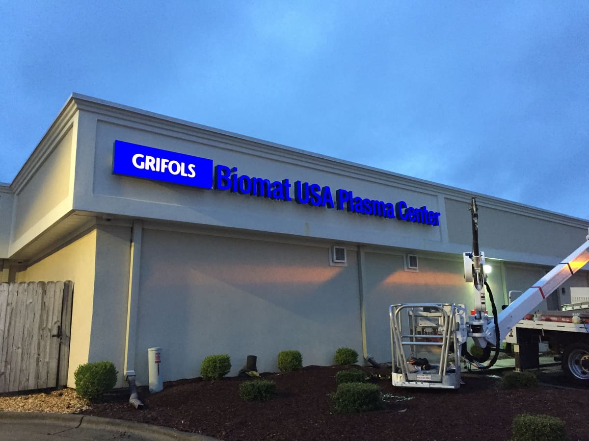 Channel letter cabinet install at dusk with bucket truck at Grifols Biomat USA Plasma Center