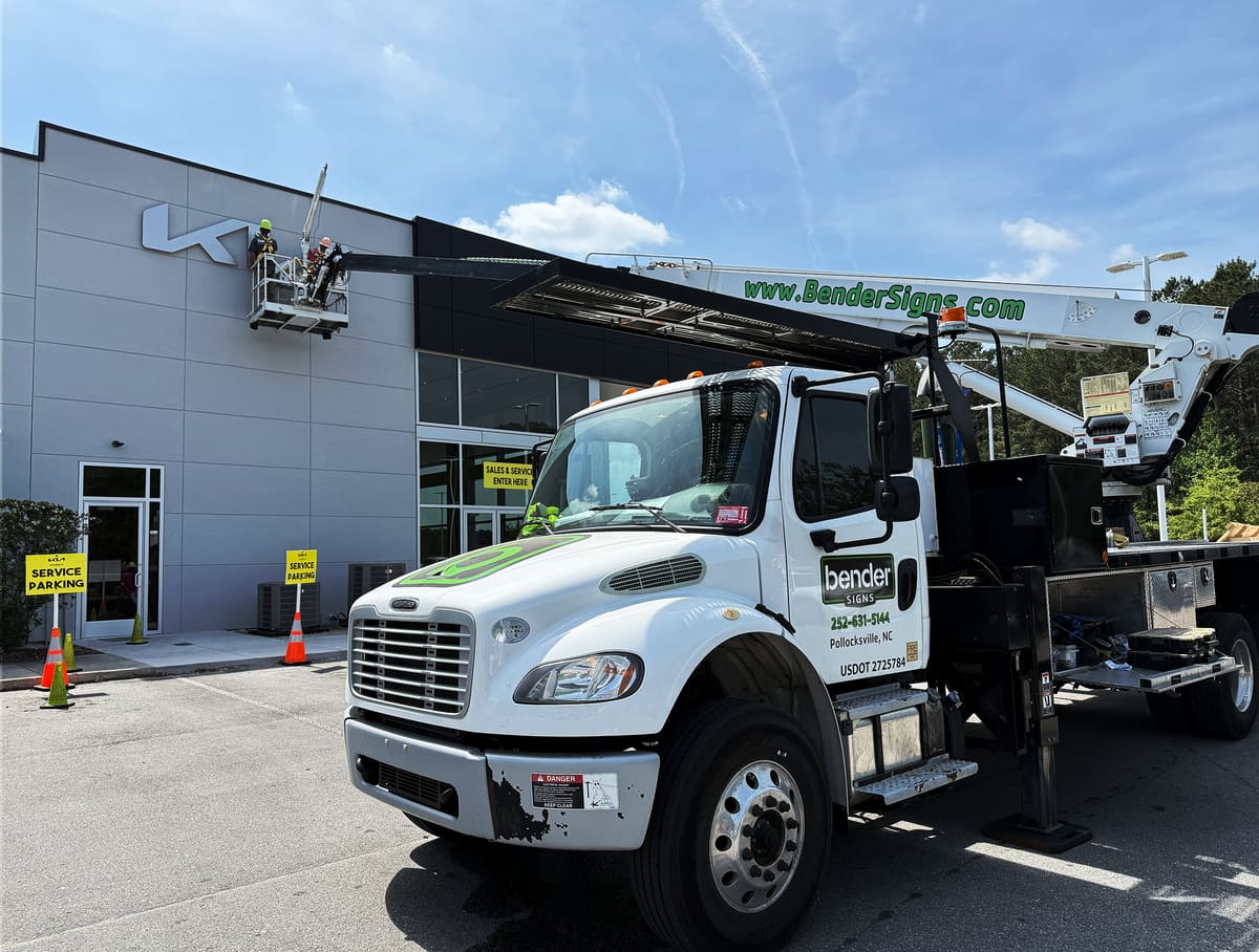 Bender crane truck with crew in the bucket at a Kia dealership facade