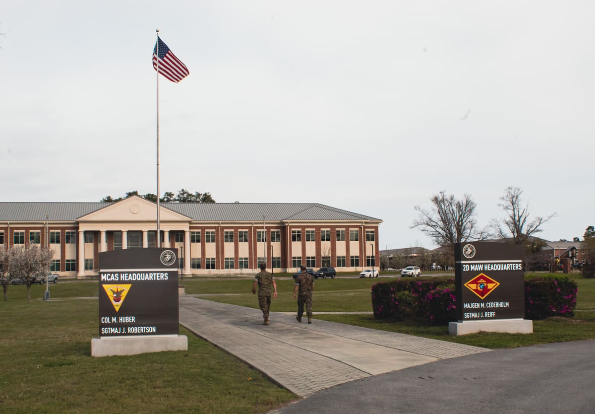 MCAS Headquarters and 2D MAW Headquarters signs with Marines walking past and the US flag