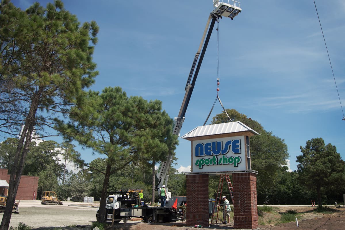 Crane setting the Neuse Sport Shop brick-base pylon cabinet among pine trees