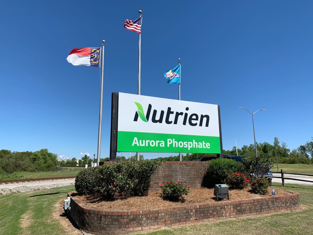 Nutrien Aurora Phosphate entrance monument sign on a brick planter base with flag poles