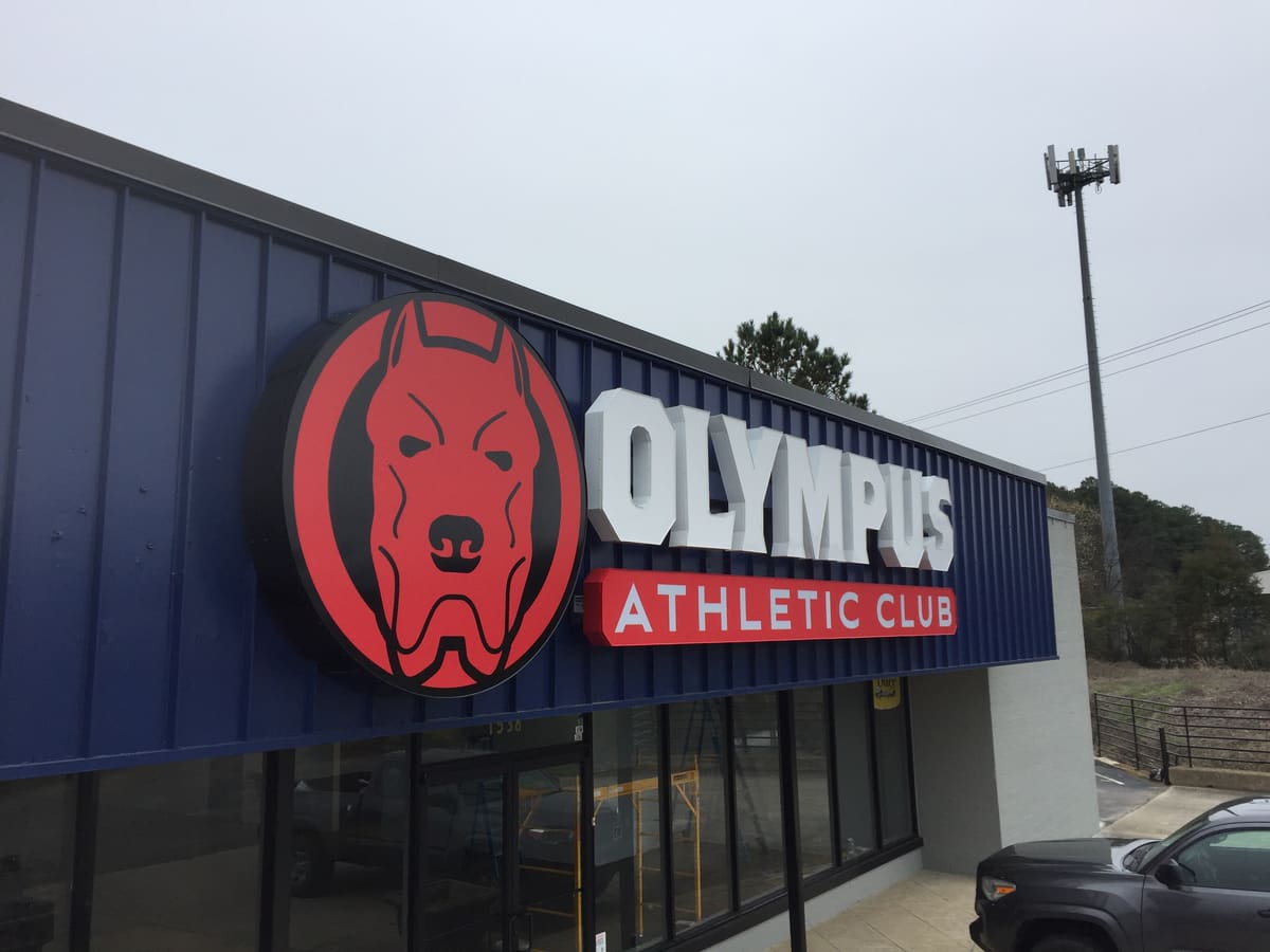 Olympus Athletic Club channel letters and round dog-logo cabinet on a blue metal facade