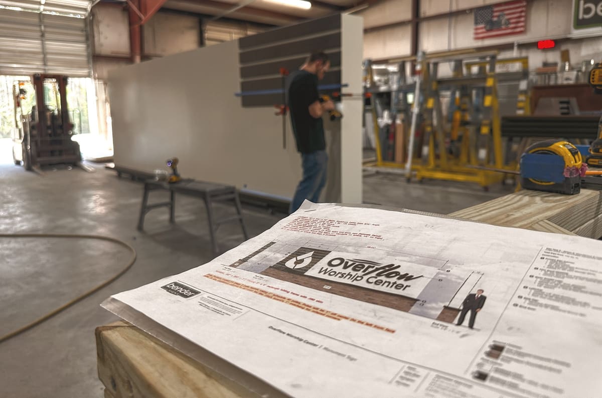 Overflow Worship Center design proof in the foreground while a fabricator builds the sign behind it