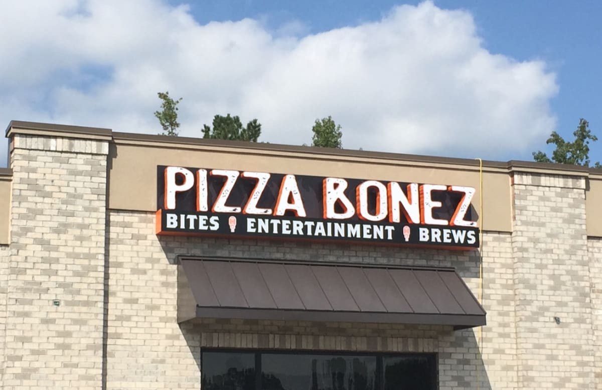 Pizza Bonez channel letters with tagline cabinet on a brick facade