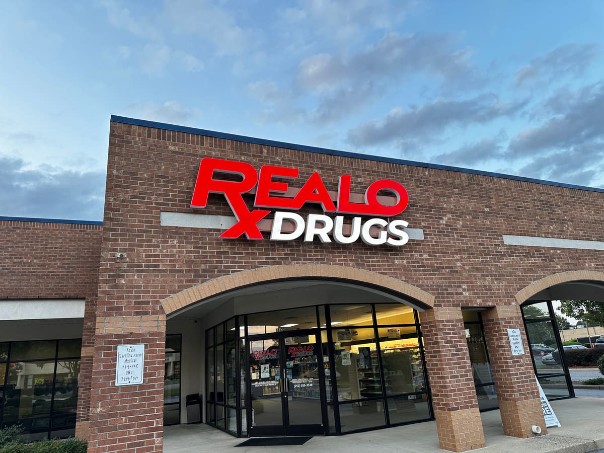 Realo Drugs red channel letters on a brick storefront at dusk