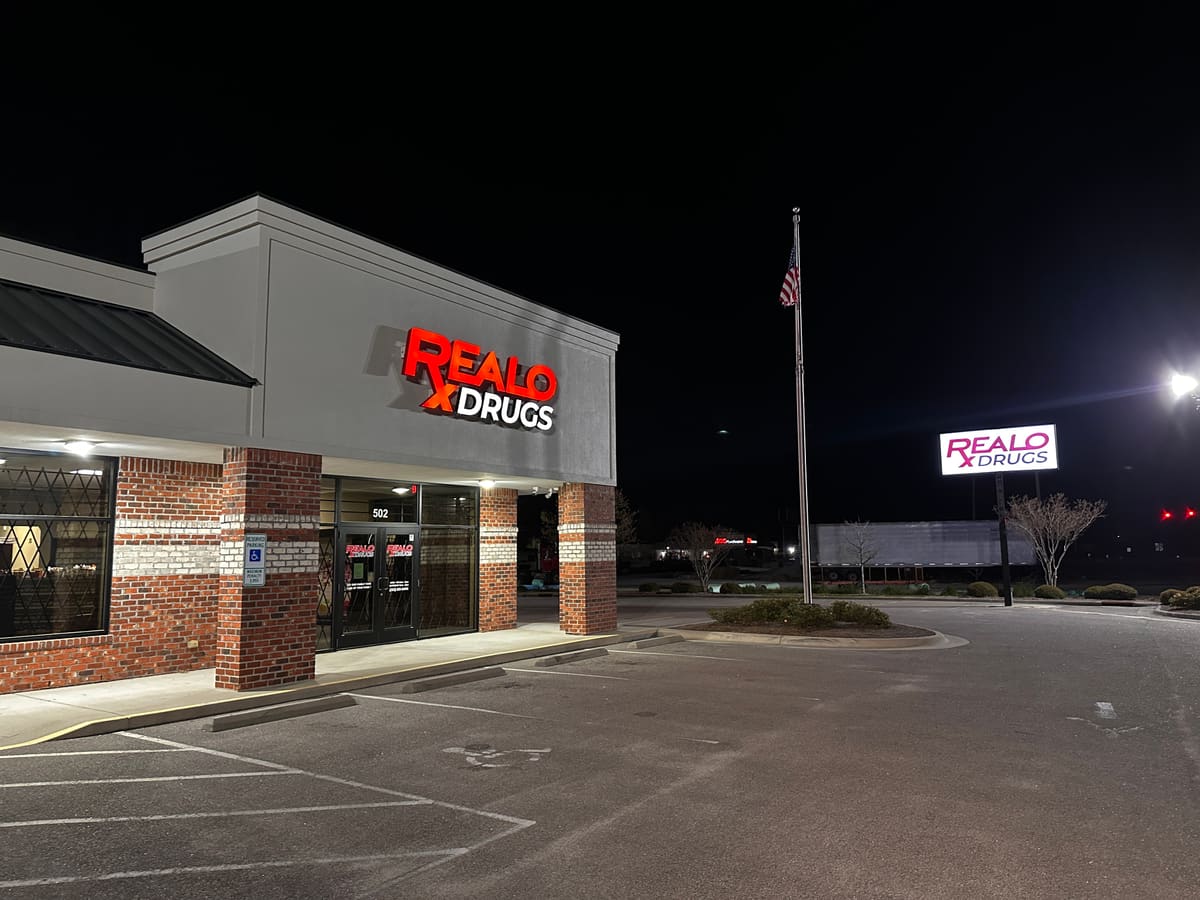 Realo Drugs storefront with lit channel letters and roadside sign at night