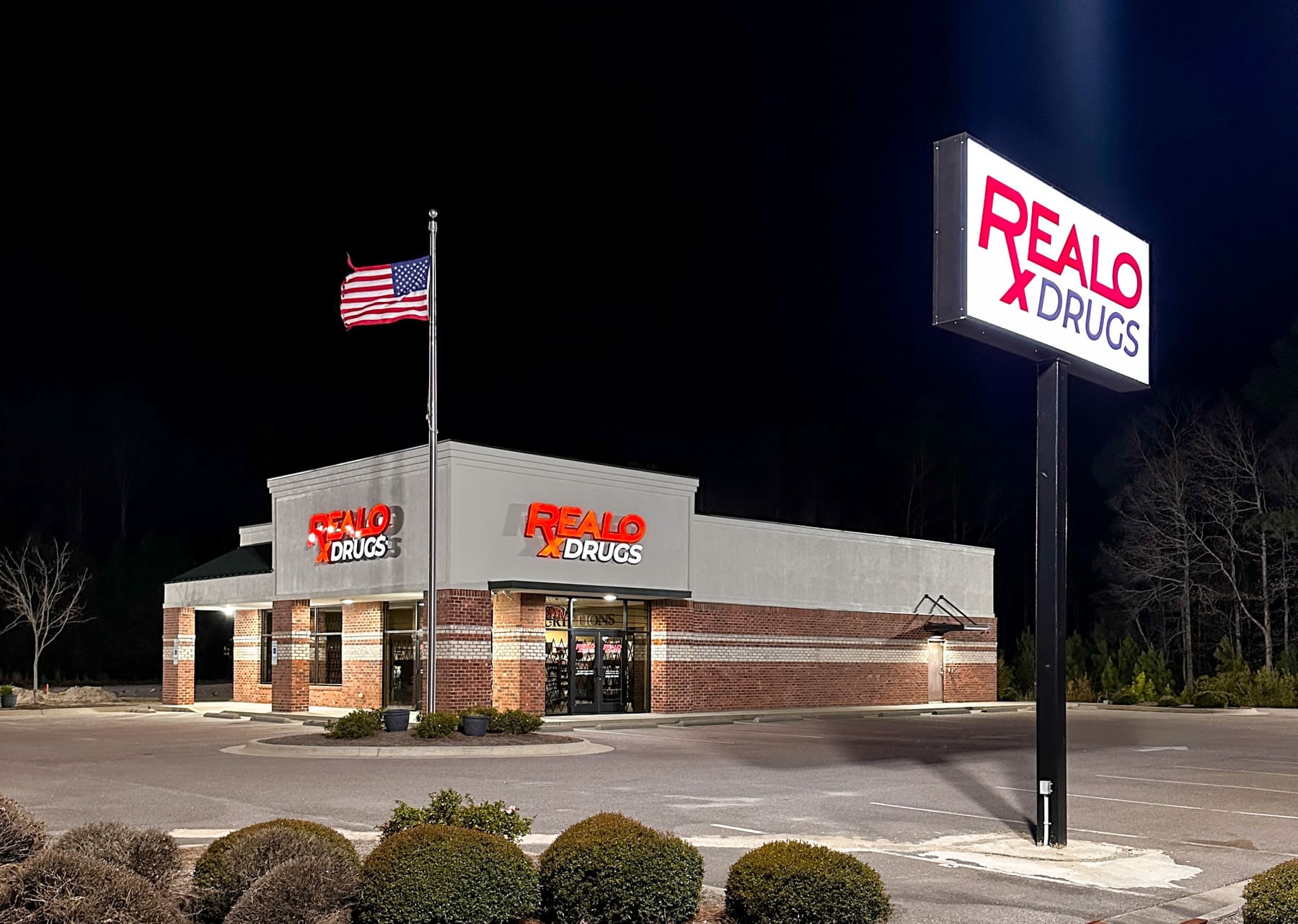 Realo Drugs storefront at night with illuminated channel letters and lit pole sign
