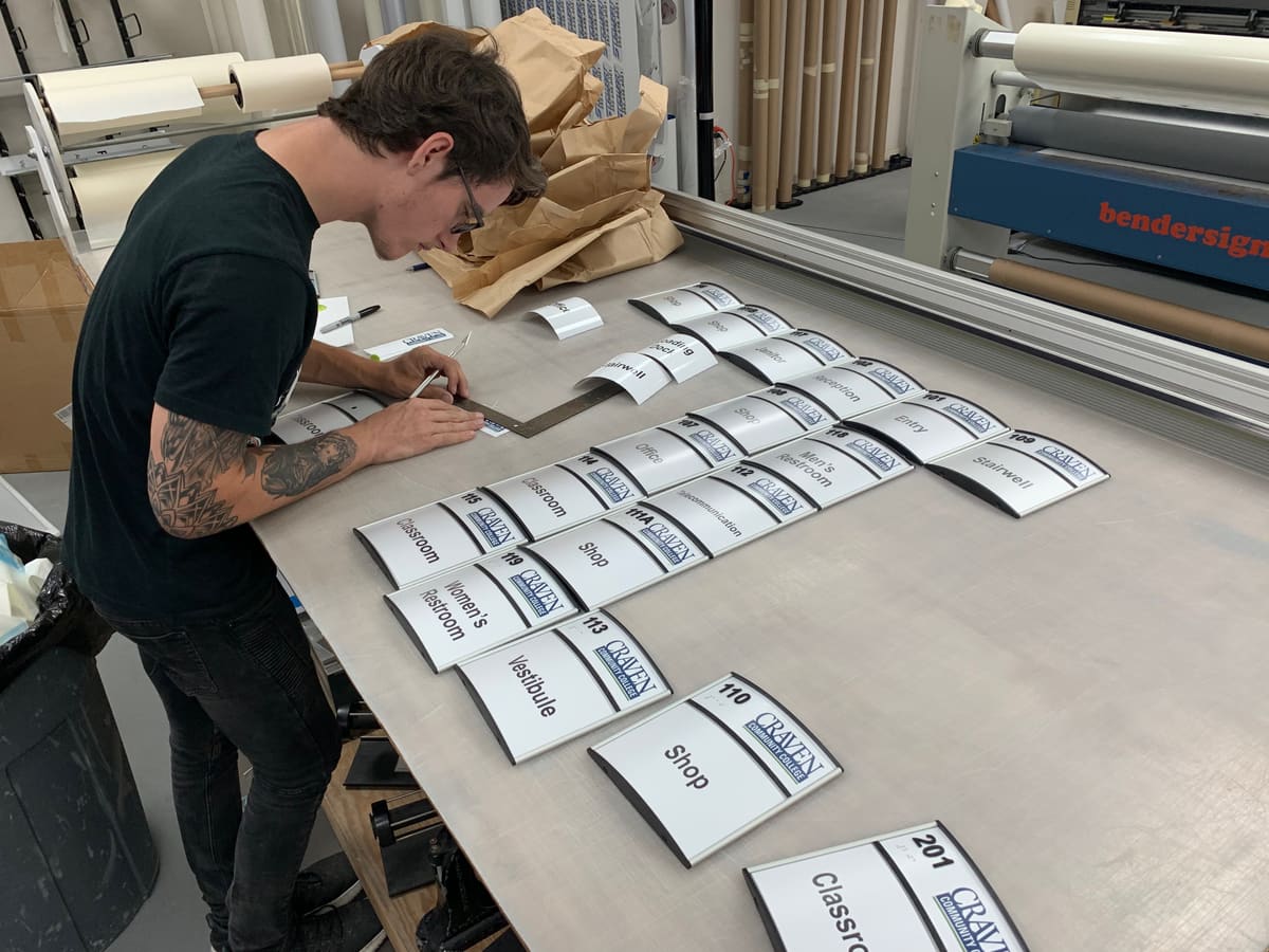 Technician assembling dozens of curved-face room ID signs on the shop table