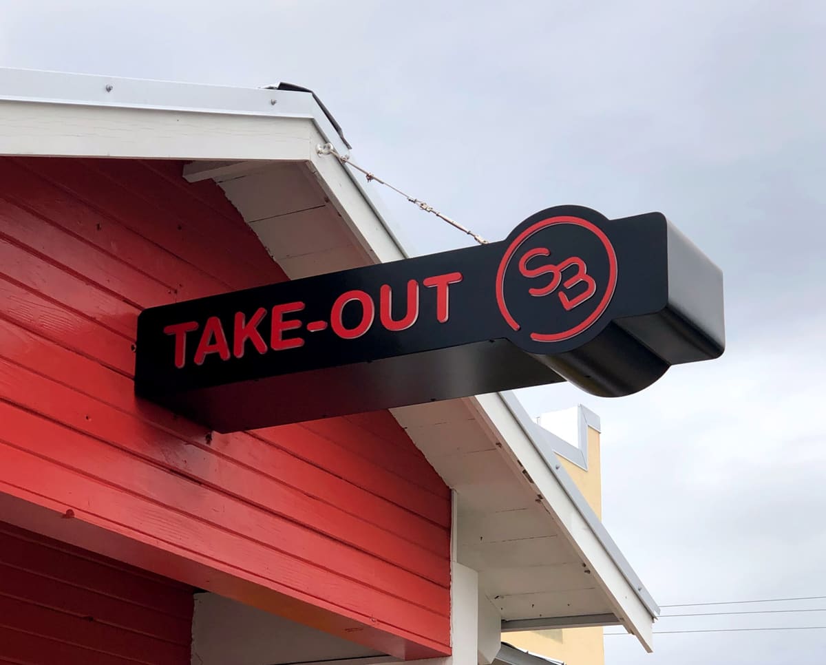 Black TAKE-OUT blade sign with monogram on a red gable