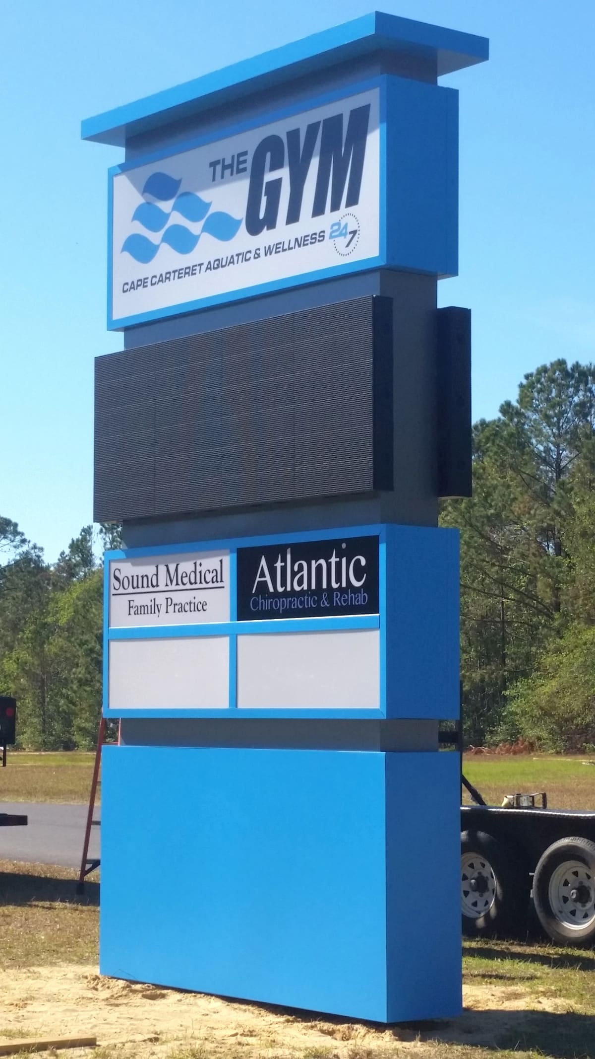 The GYM blue pylon sign with LED board and tenant panels in daylight