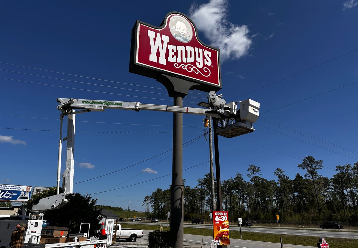 Bender bucket truck crew servicing a Wendy’s pylon sign against a deep blue sky